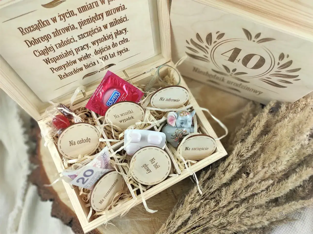 Drewniana skrzynka z prezentami na 40. urodziny: prezerwatywa, słodycze, figurka słonia, leki, pieniądze i ozdobne krążki.