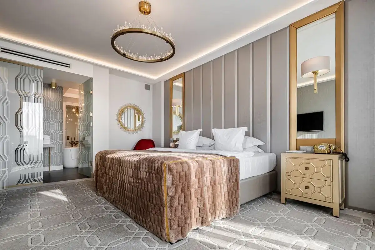 Elegancki pokój hotelowy 4-gwiazdkowy spełniający wysokie wymagania: łóżko z puszystym kocem, kryształowy żyrandol, złote lustra i stylowe meble.