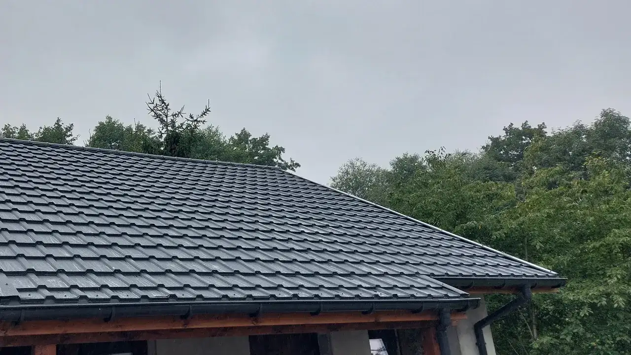 Szary dach z blachy, idealny przykład, jak uszczelnić dach przed deszczem. Wokół zielone drzewa.