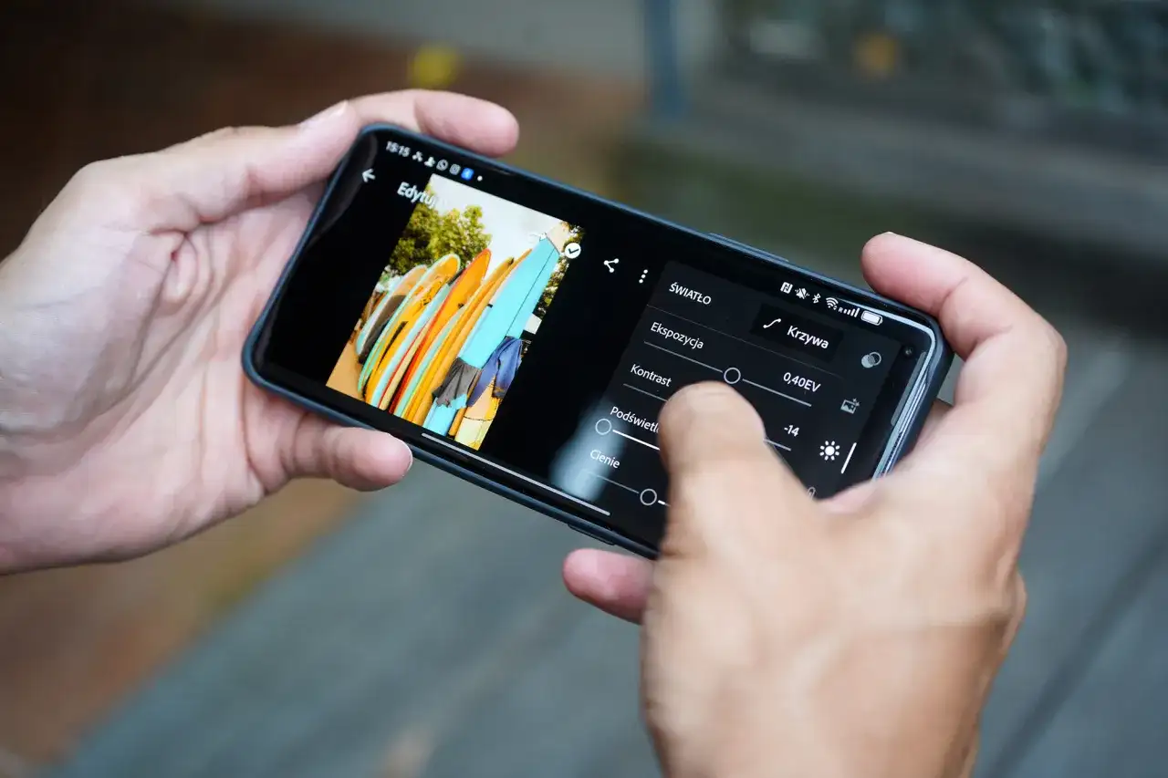 Ręce trzymają smartfon, na którym widać edycję zdjęcia desek surfingowych. Dowiedz się, jak zrobić zdjęcie z filmu na telefonie, edytując je.