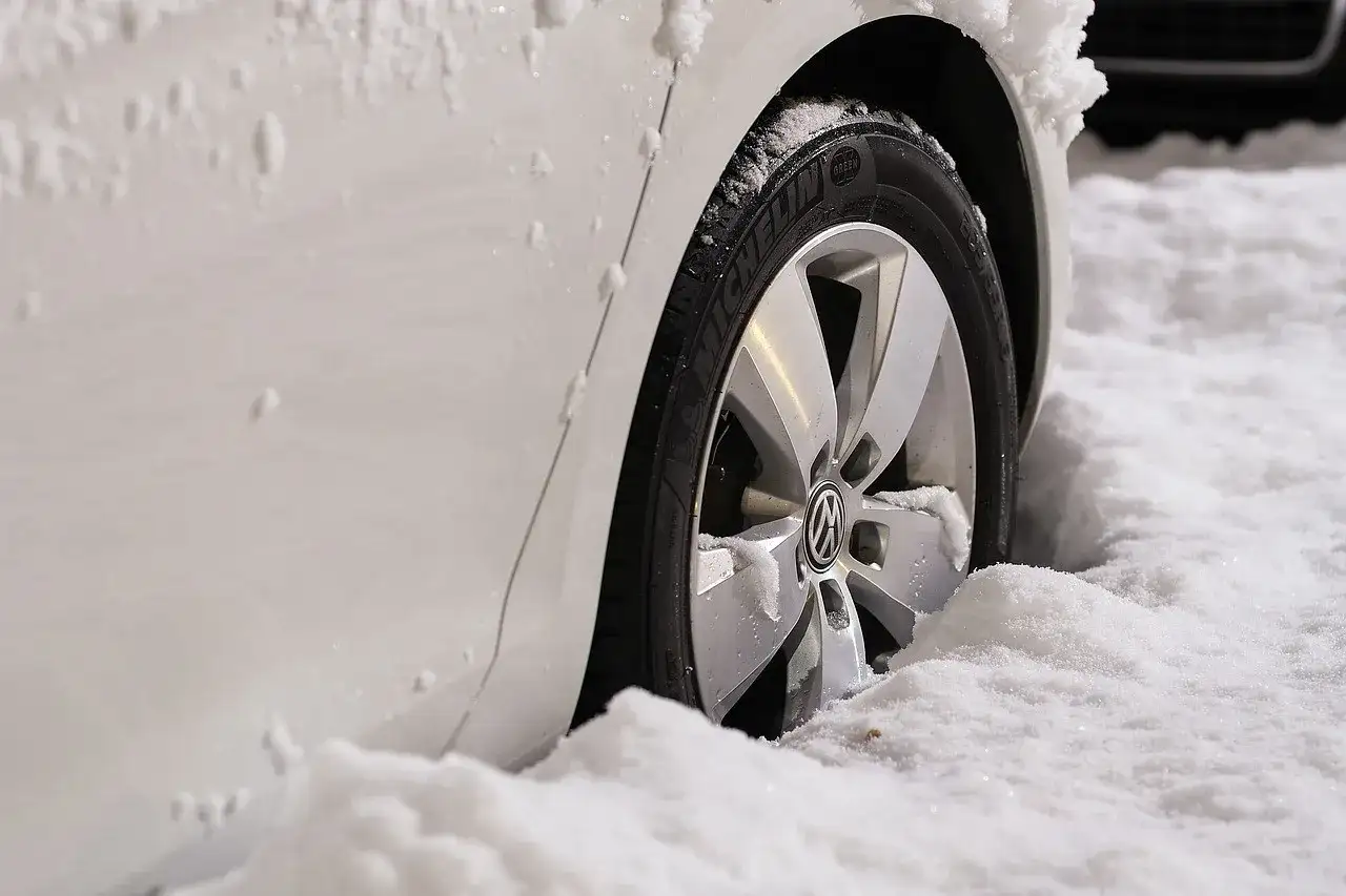 Biały samochód z felgami i oponami Michelin w śniegu. Zastanawiasz się, jakie opony zimowe wybrać?