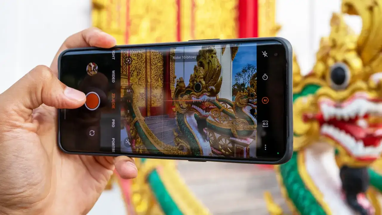 Dłoń trzyma smartfon, na ekranie którego widać smoka i złote zdobienia. Tak właśnie można zacząć przygodę, jak zrobić dobre zdjęcie telefonem.
