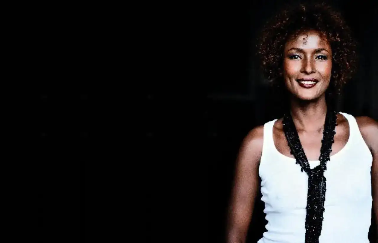 Waris Dirie w białej koszulce i czarnym naszyjniku, uśmiecha się.