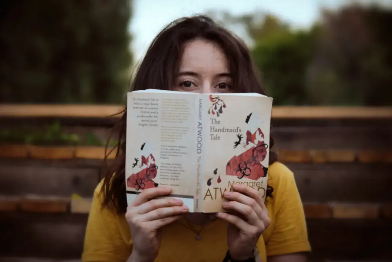 Dziewczyna w żółtej bluzce czyta książkę po angielsku "The Handmaid's Tale" Margaret Atwood.