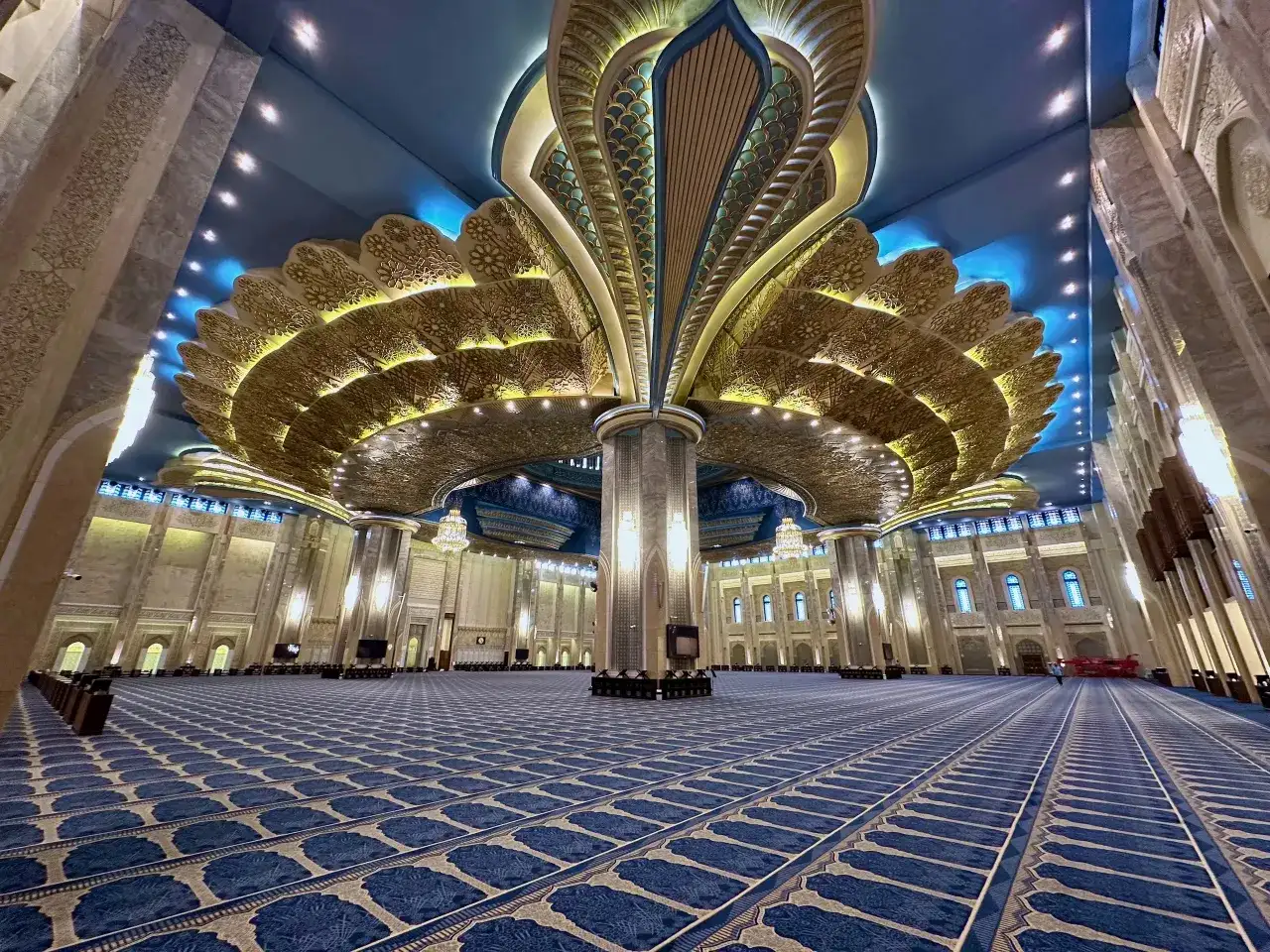 Wnętrze Wielkiego Meczetu w Kuwejcie z ozdobnym sufitem i niebieskim dywanem.