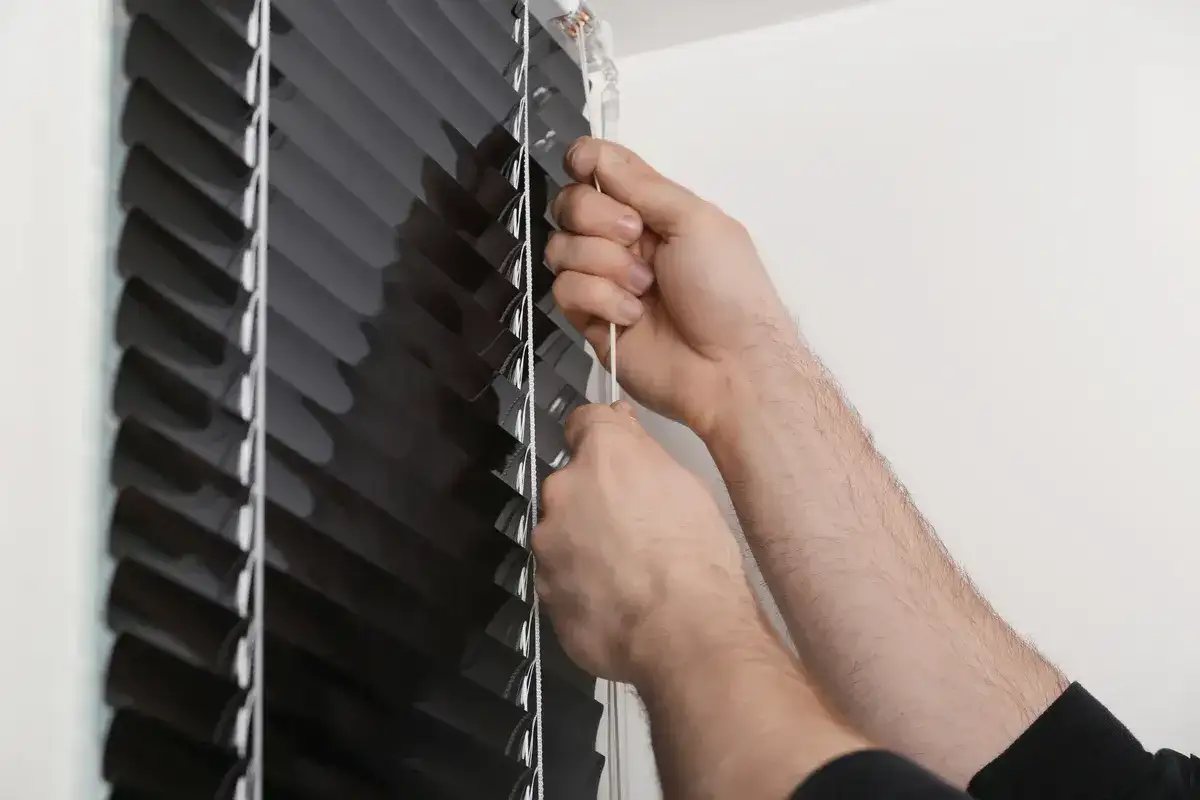 Dłonie regulują czarną roletę, pociągając za białą taśmę.