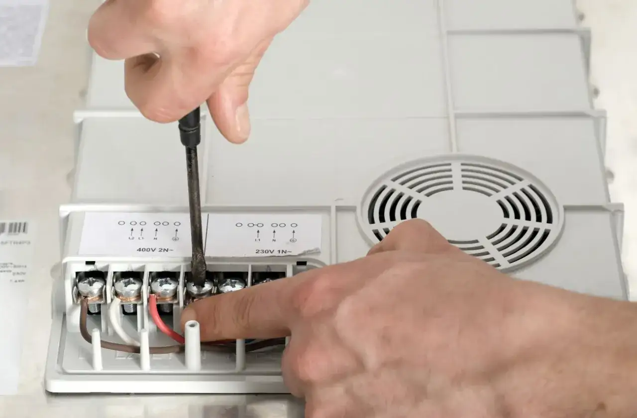 Ręce majsterkowicza podłączają przewód do płyty indukcyjnej, dokręcając śruby śrubokrętem.