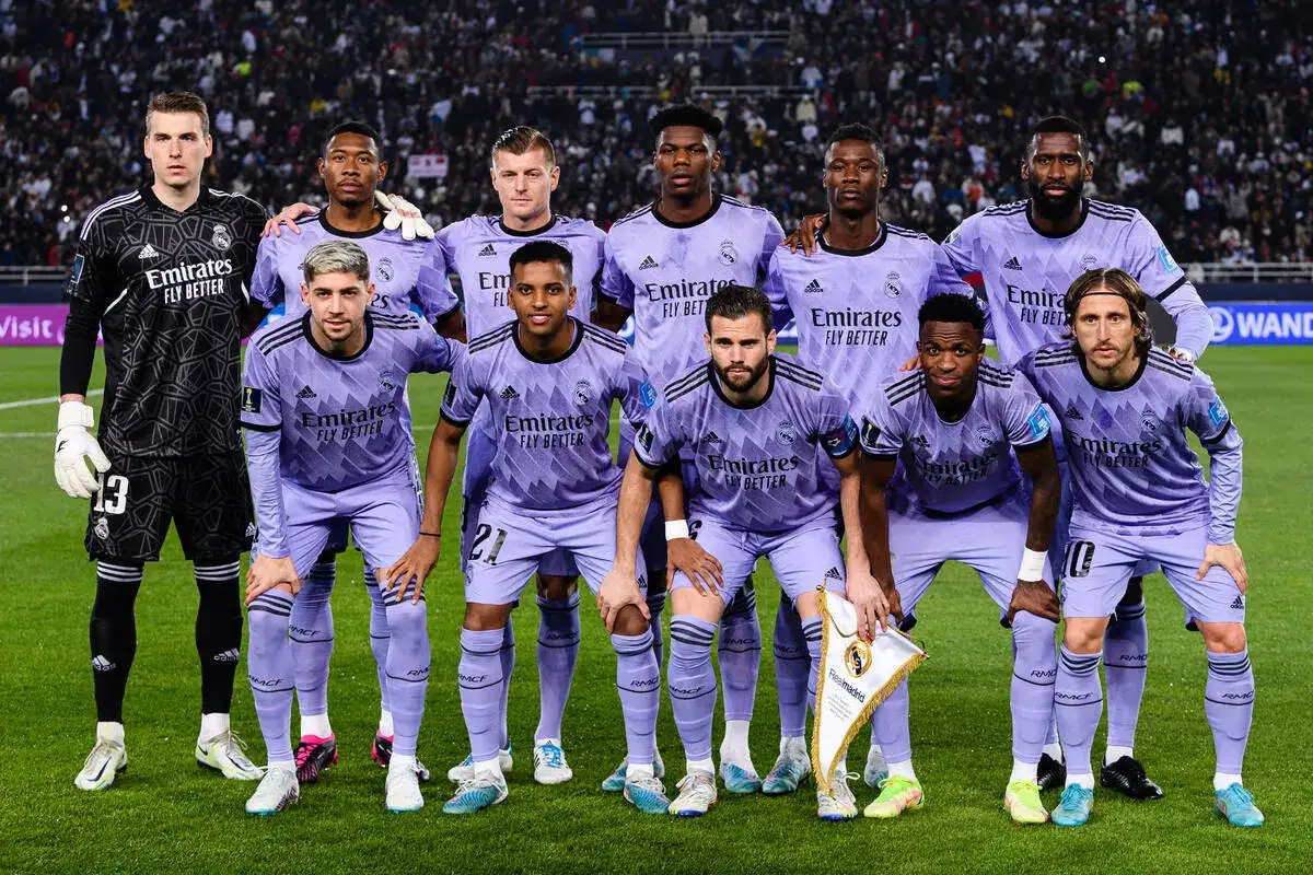 Drużyna pilkarze Real Madryt w fioletowych strojach pozuje do zdjęcia na murawie stadionu.
