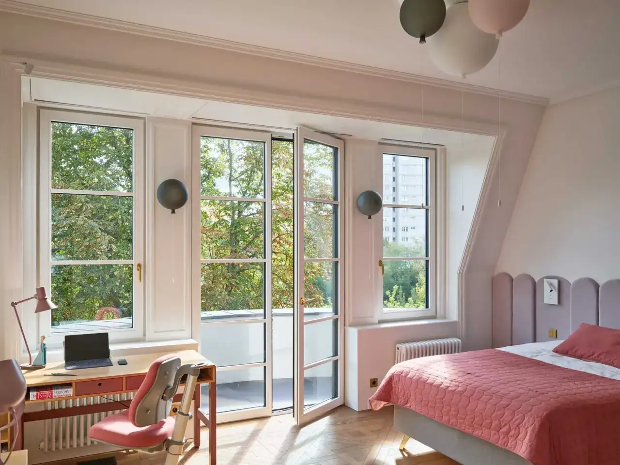 Uroczy pokój z biurkiem i łóżkiem. W tle duże okna z widokiem na drzewa, a na nich wiszą dekoracyjne opaski wokół okien w kształcie balonów.