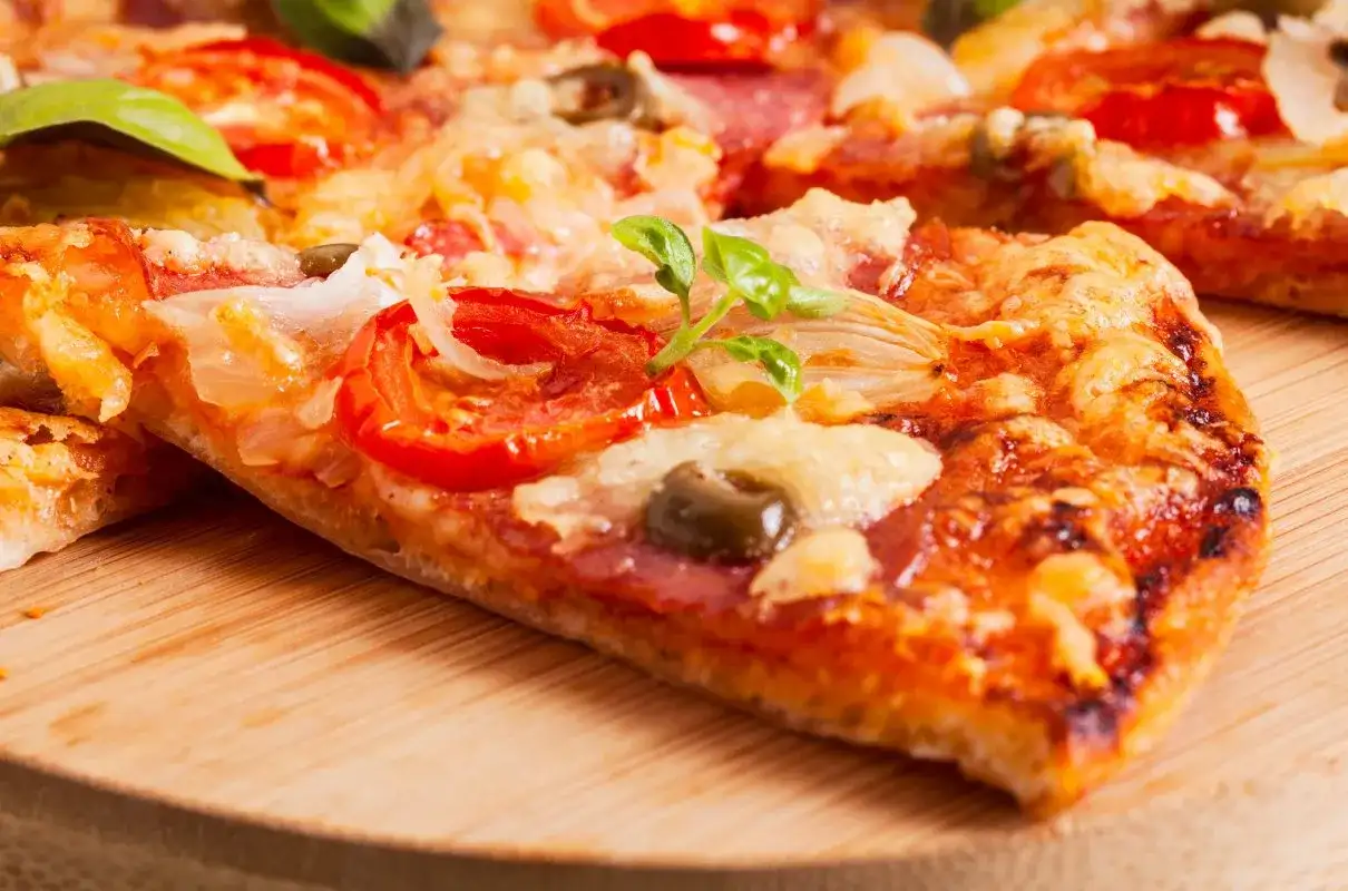 Pyszna pizza na serku wiejskim z pomidorami, oliwkami i bazylią, podana na drewnianej desce.