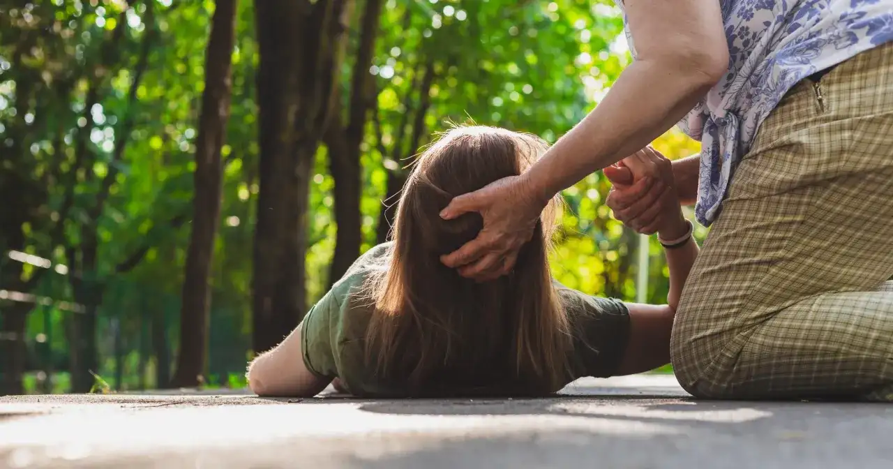 Osoba na ziemi, być może doświadczająca nietypowych objawów padaczki, otrzymuje pomoc od drugiej osoby.