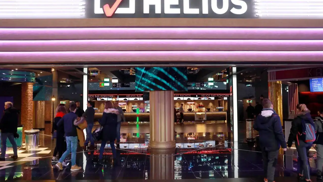 Ludzie wchodzą do kina Helios. Zastanawiasz się, ile kosztuje średni popcorn w Heliosie? Warto sprawdzić ceny przy barze.
