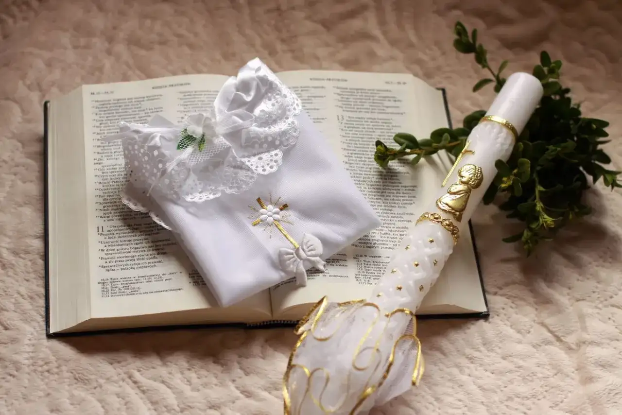 Biała szatka i paschalna świeca na otwartej Biblii. Symbole chrztu i ich znaczenie, światło wiary i czystość.