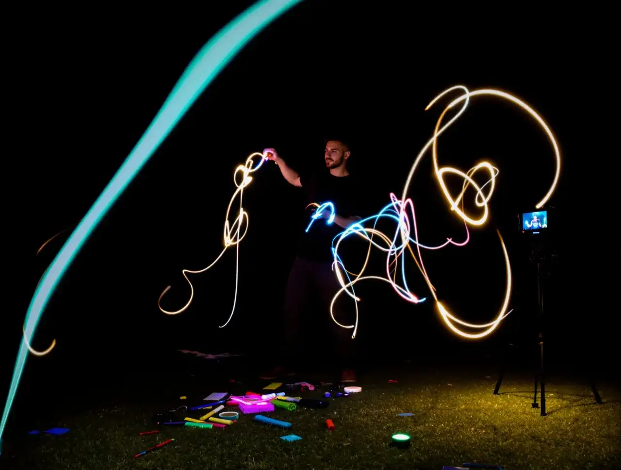 Artysta tworzy świetlne malowidła, wykorzystując zaawansowane techniki fotograficzne. Kolorowe smugi światła wirują wokół postaci na tle ciemnego nieba.