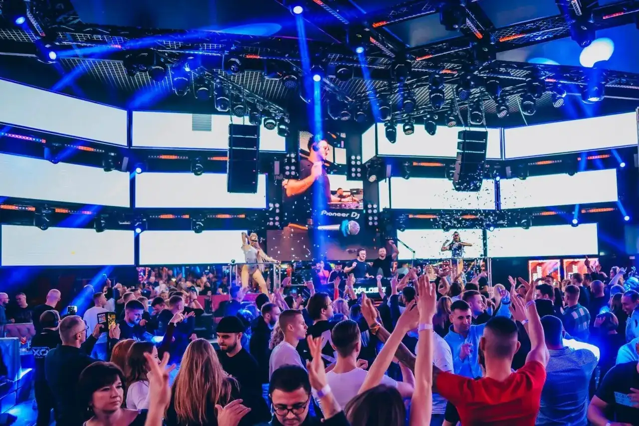 Koncert DJ-a w klubie z tłumem bawiących się ludzi i efektami świetlnymi.