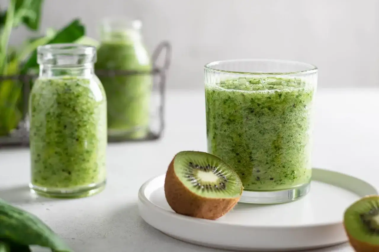 Zielony koktajl w szklance i butelkach, z połówkami kiwi na talerzyku.