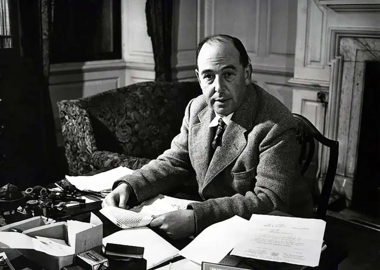 C.S. Lewis, autor "Opowieści z Narnii", siedzi przy biurku, otoczony papierami i atramentem.
