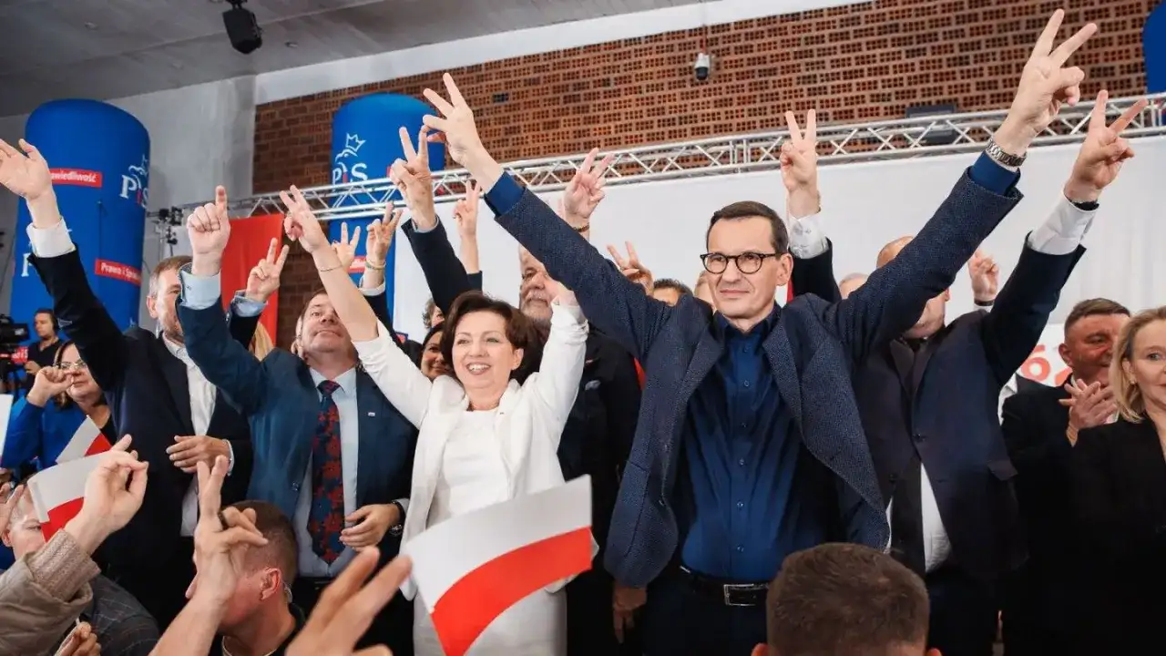 Radosny tłum z polskimi flagami i znakami zwycięstwa. W centrum Mateusz Morawiecki i inni politycy PiS, być może świętujący sukces, mimo że lista afer PiS jest długa.