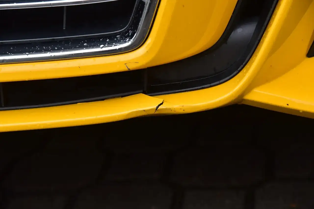 Żółty zderzak samochodu z pęknięciem i zarysowaniami.