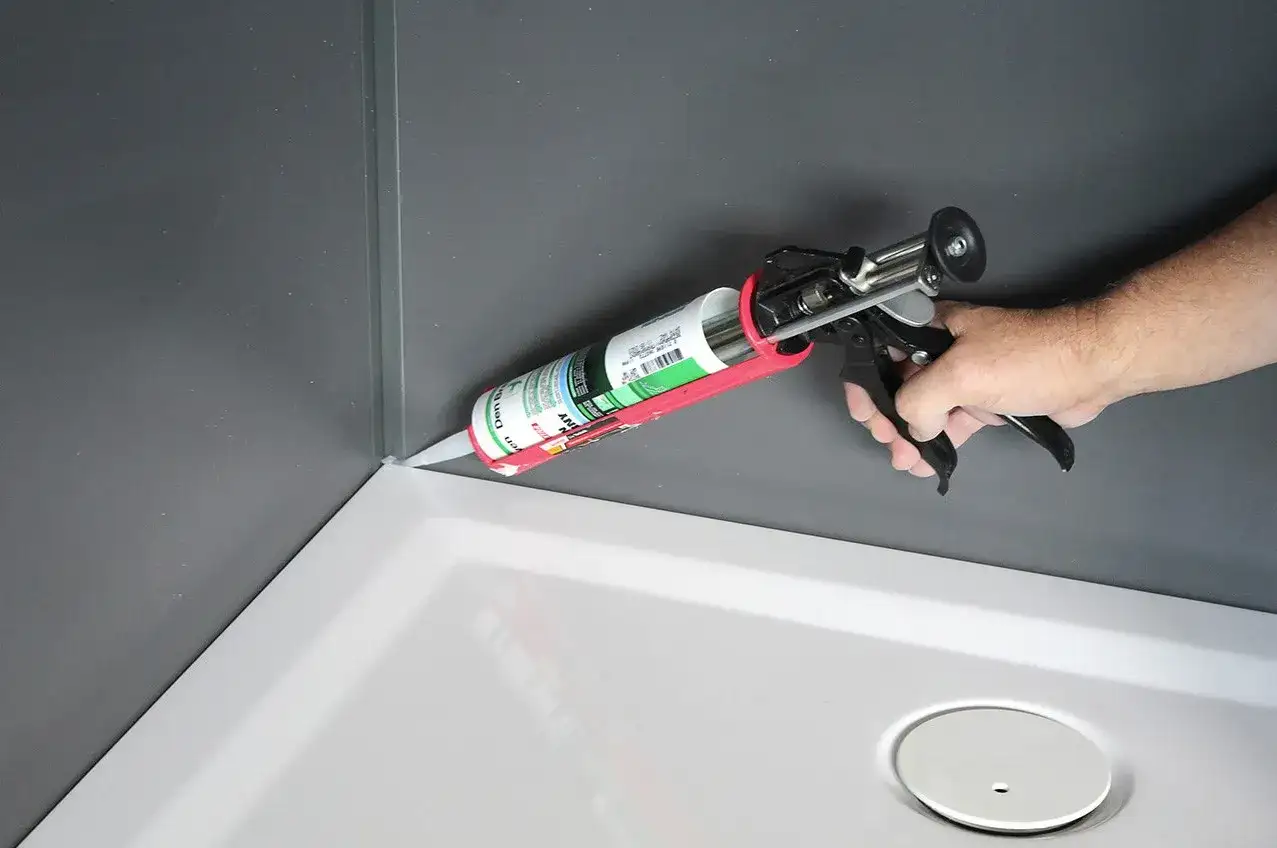 Nakładanie silikonu do kabiny prysznicowej w rogu brodzika.