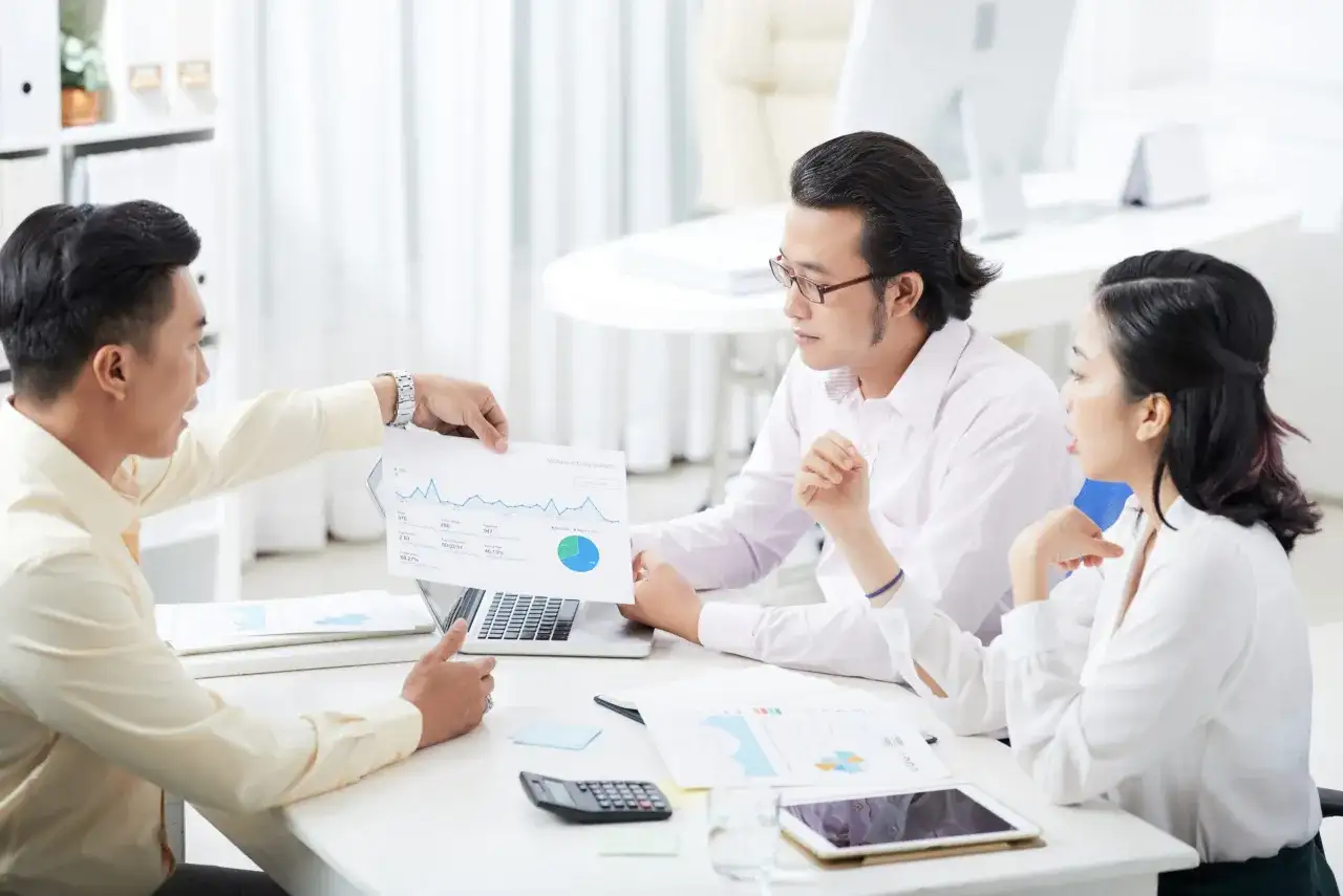 Zespół analizuje dane, omawiając potencjalną cesję polisy. Na stole leżą dokumenty, laptop i kalkulator.