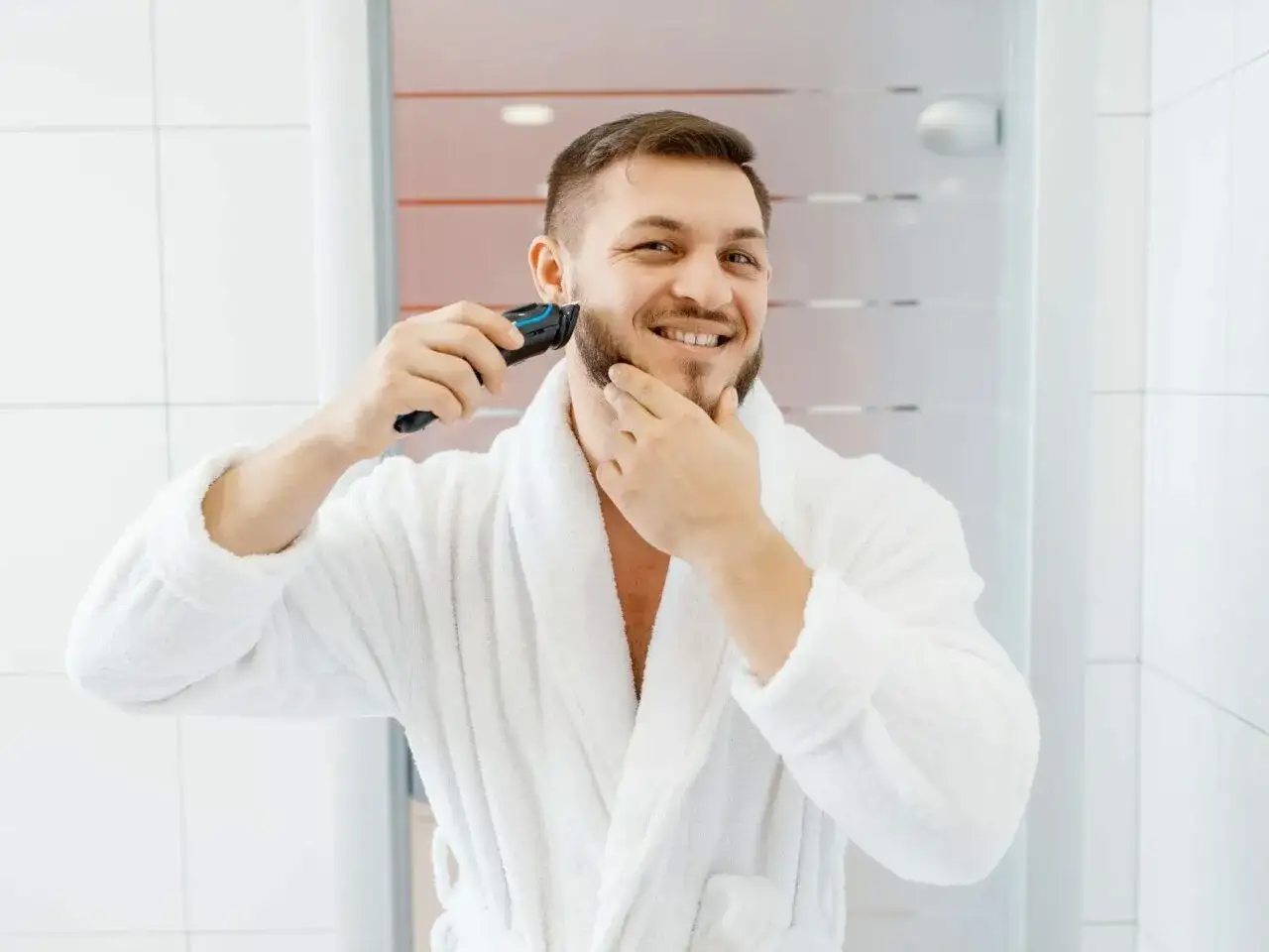 Mężczyzna w białym szlafroku goli zarost trymerem.