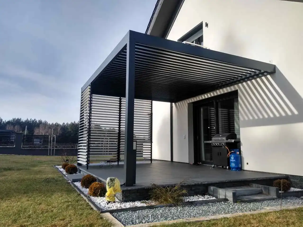 Nowoczesna pergola z ruchomymi lamelami i grillem obok. Zastanawiasz się, ile kosztuje zrobienie pergoli?