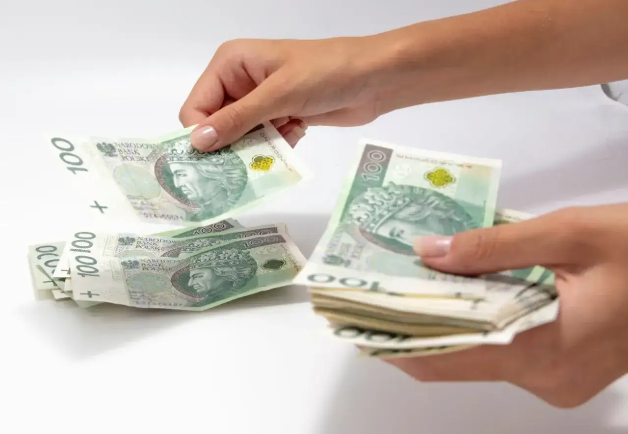 Dwie dłonie liczą banknoty 100 zł. Jakby sennik podarte rajstopy, pieniądze są rozrzucone i w stosie, symbolizując niepewność finansową.