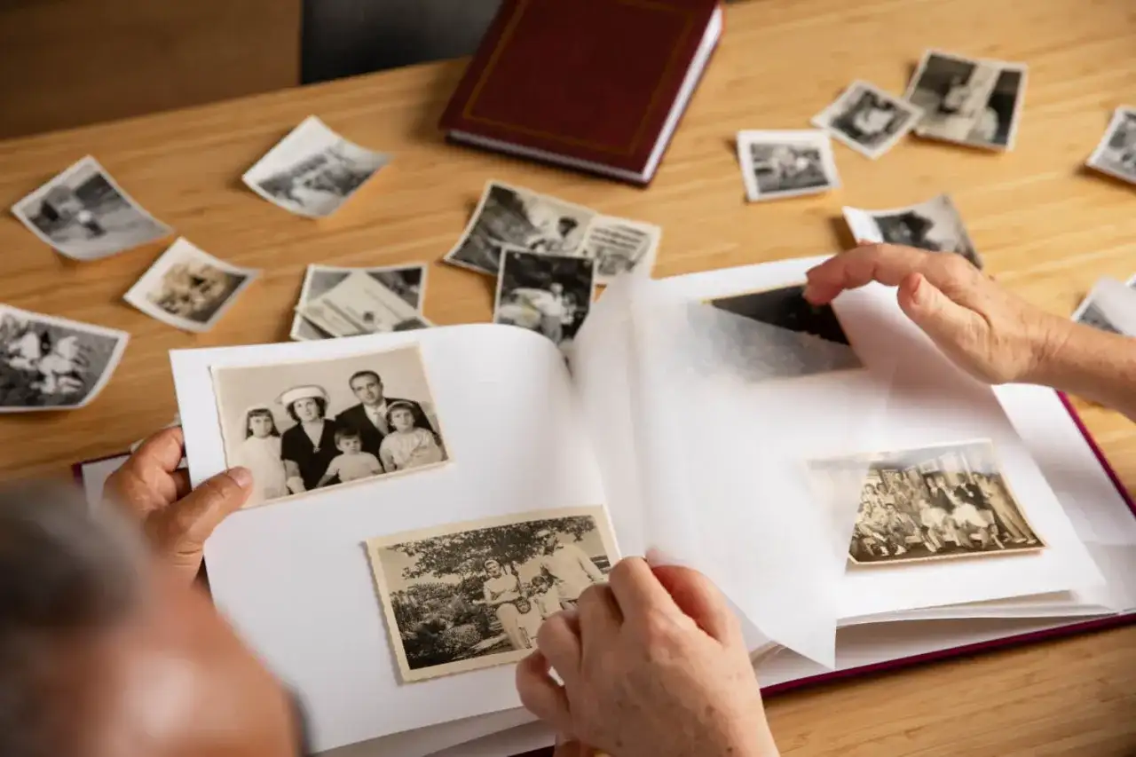 Wspomnienia wracają podczas wklejania zdjęć do albumu. Na stole leżą stare fotografie, a ręce starannie układają je na białych kartach.