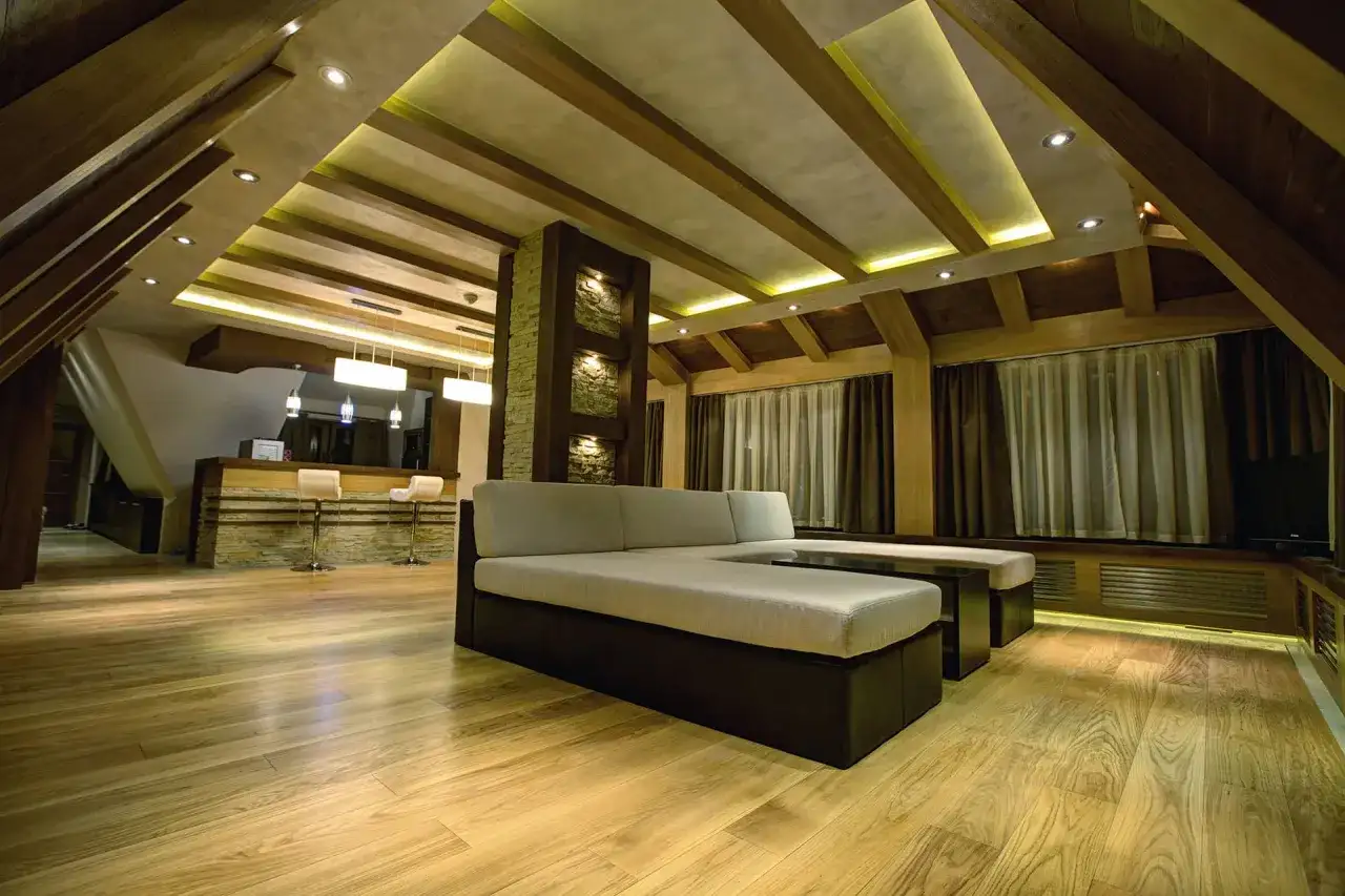 Nowoczesne wnętrze z drewnianymi belkami i ledami na skosach. Wygodny narożnik i bar tworzą przytulną atmosferę.