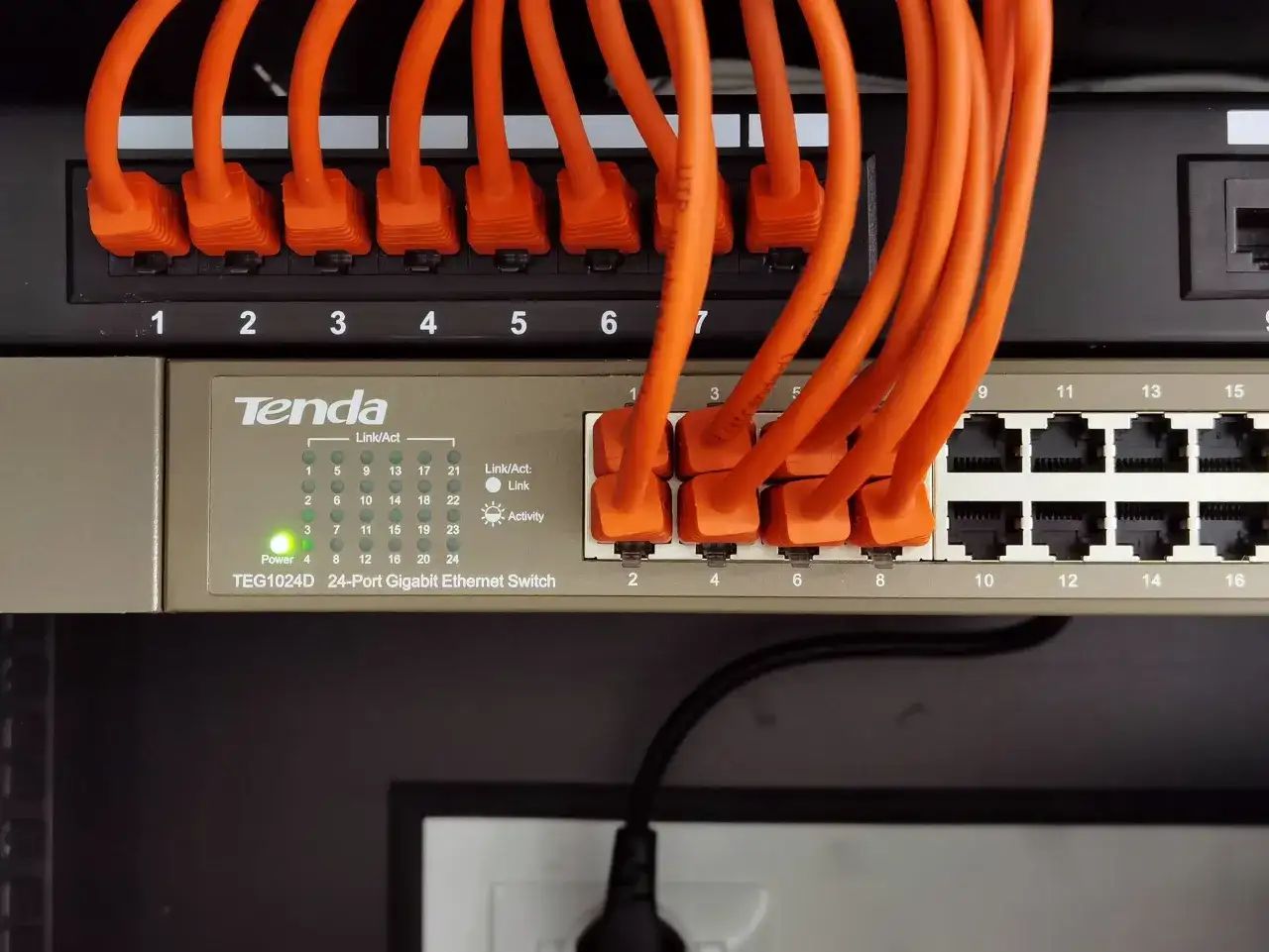 Pomarańczowe kable sieciowe podłączone do przełącznika Tenda TEG1024D, tworzące sieć LAN w domu.