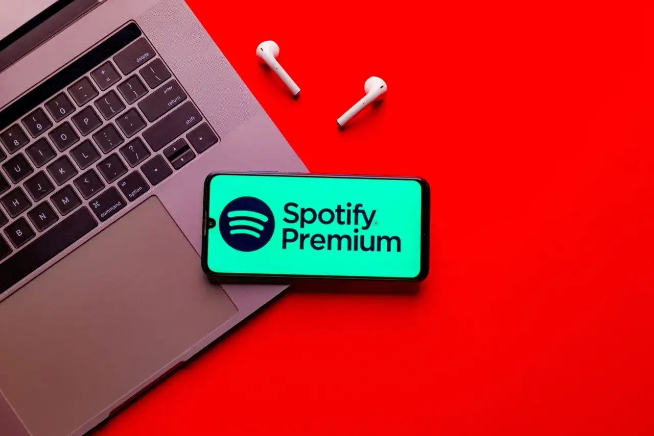 Laptop, telefon z logo Spotify Premium i słuchawki na czerwonym tle.