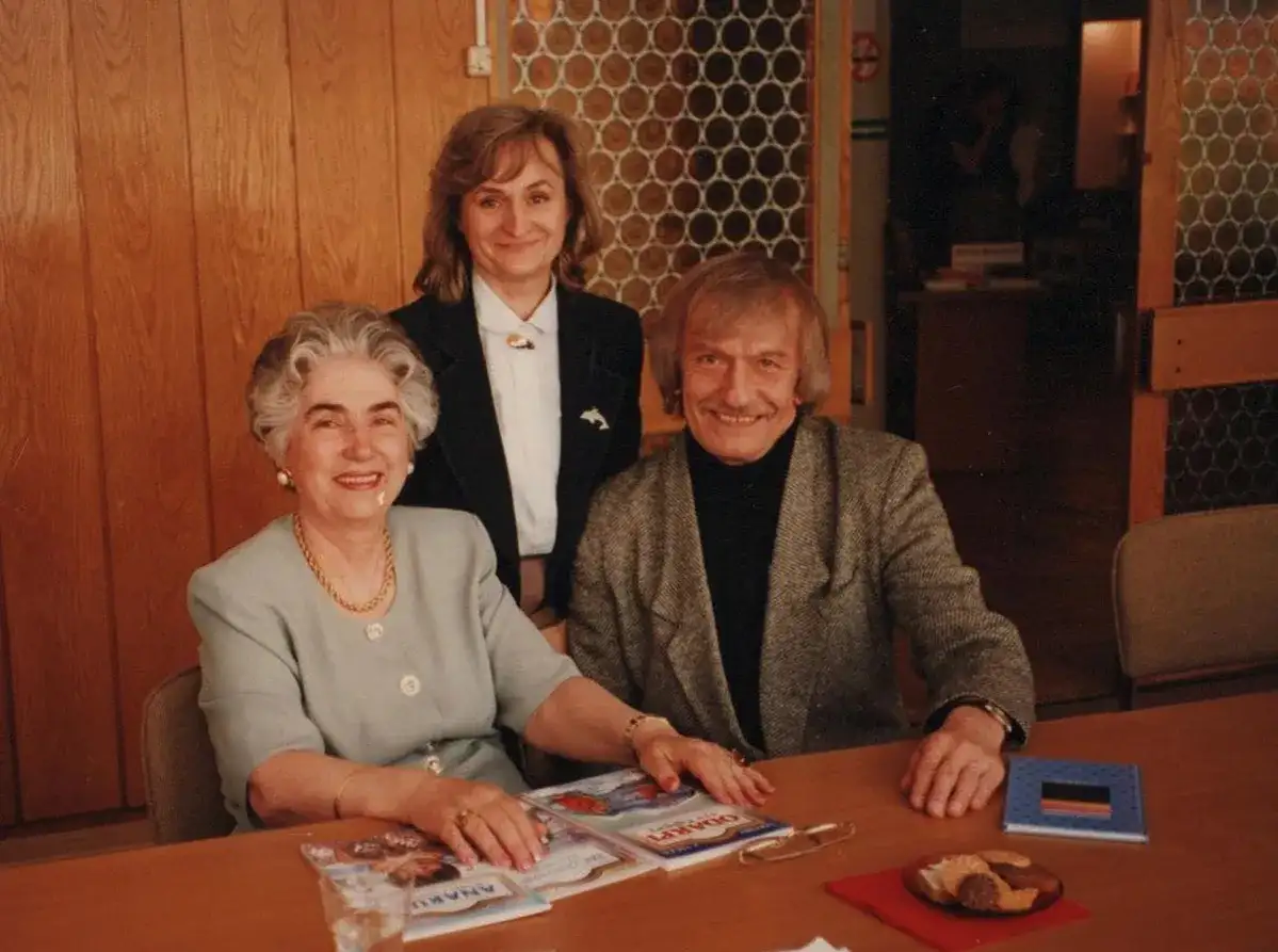 Trzy osoby przy stole. Starsza pani z siwymi włosami, młodsza kobieta i mężczyzna. Na stole książki, w tym "Zaczarowana zagroda", której autorem jest Jan Brzechwa.