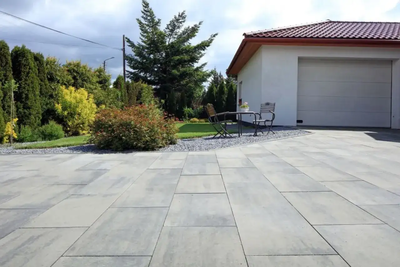 Nowe płytki na podjazd w nowoczesnym stylu. Szare, prostokątne płyty tworzą elegancką nawierzchnię przed domem z garażem.