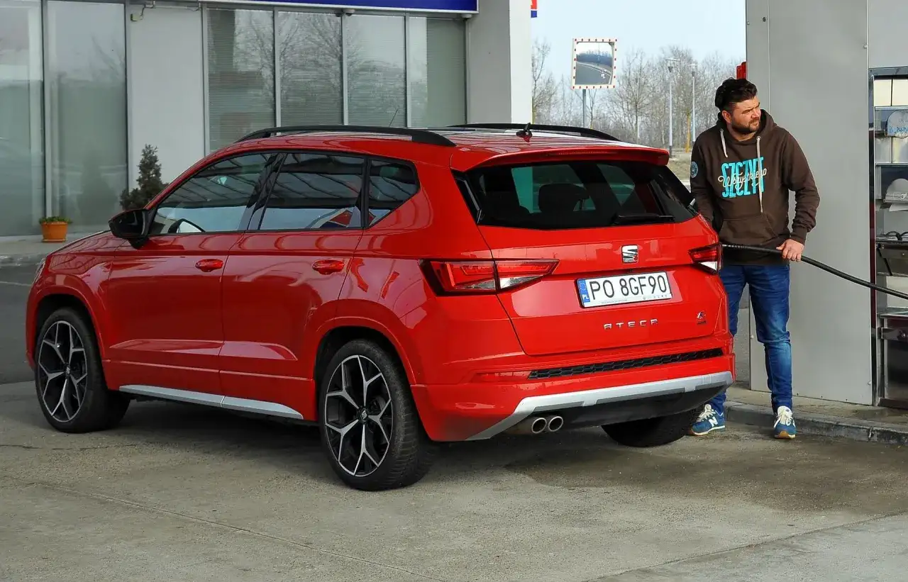 Mężczyzna tankuje czerwonego SUV-a. Zastanawiasz się, ile pali suv? Ten model Seat Ateca właśnie dostaje paliwo.