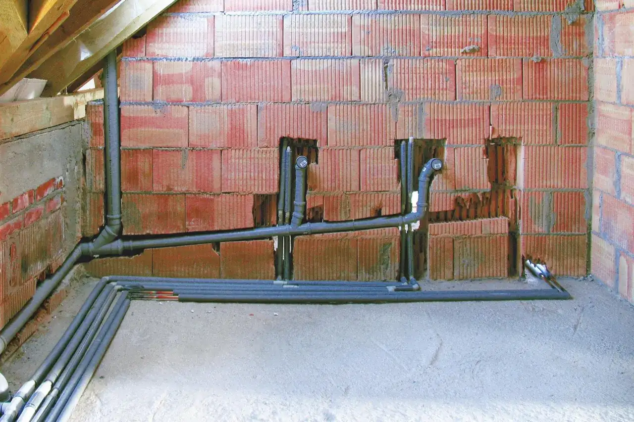 Instalacja hydrauliczna z rurami, zapewniająca minimalny spadek dla rury 160. Ściana z pustaków ceramicznych, podłoga betonowa, widoczne drewniane elementy konstrukcji dachu.