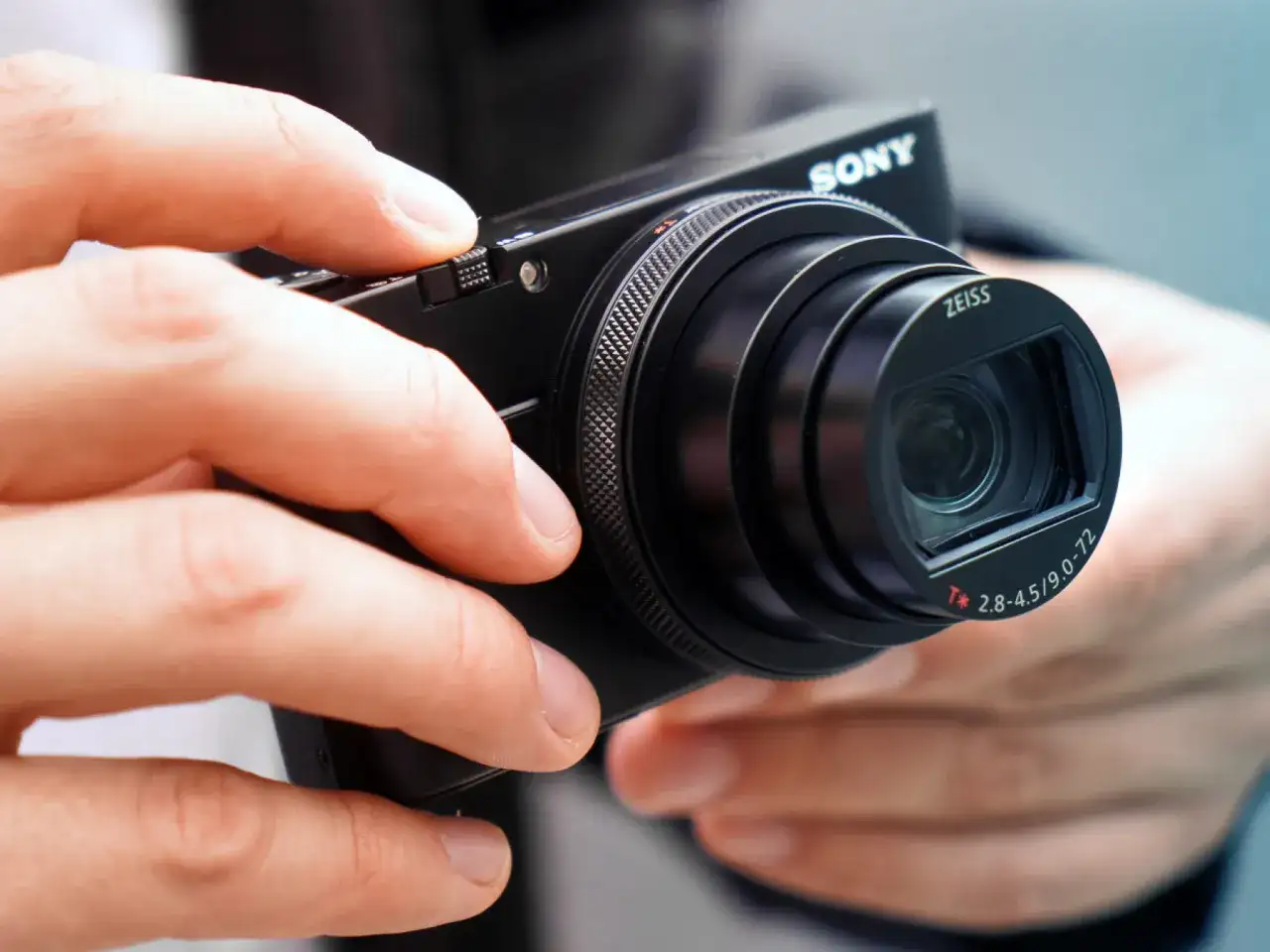 Dłonie trzymają aparat Sony RX100 VII z obiektywem Zeiss.