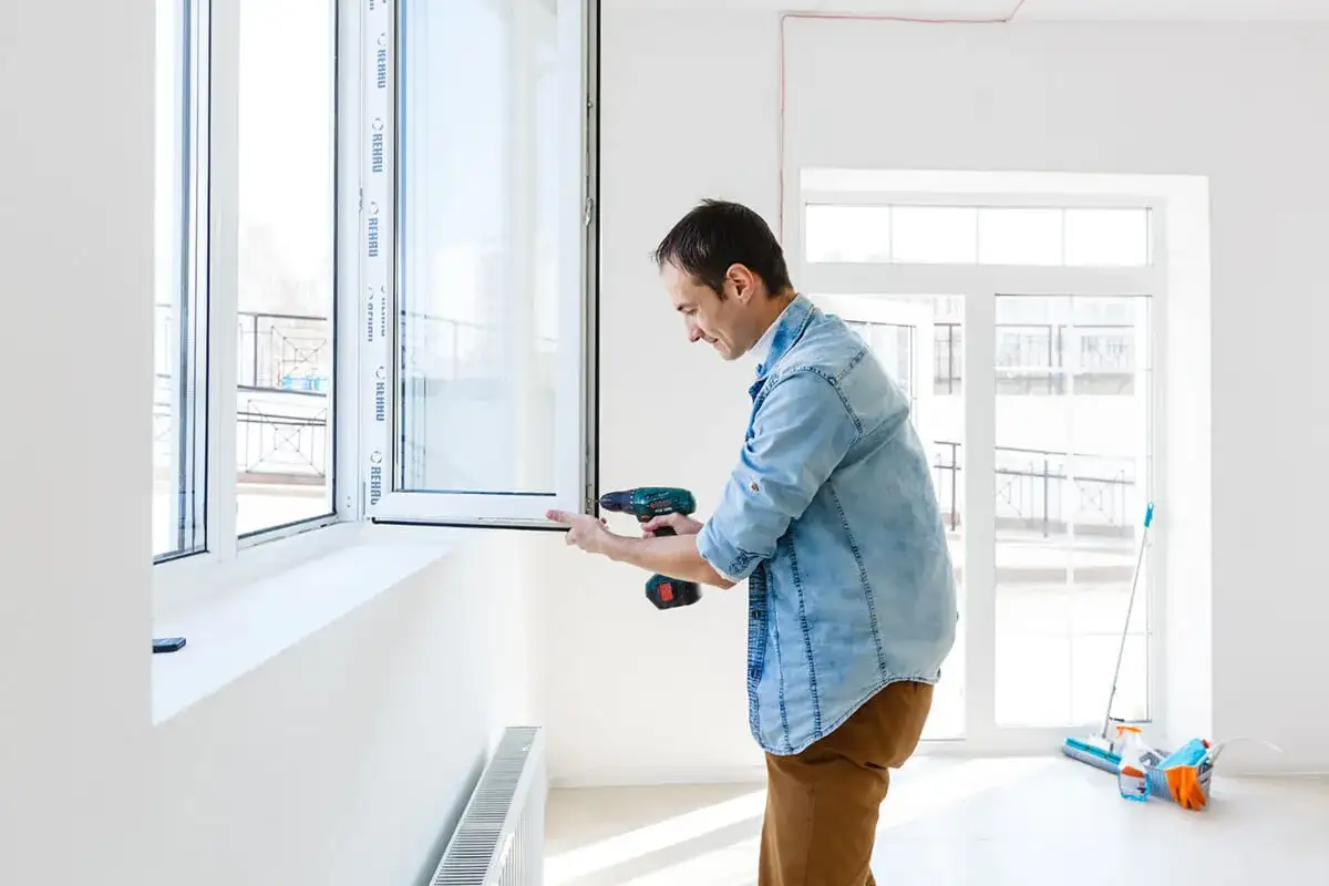 Mężczyzna montuje okno, co może pomóc oszacować, ile kosztuje wstawienie okna.