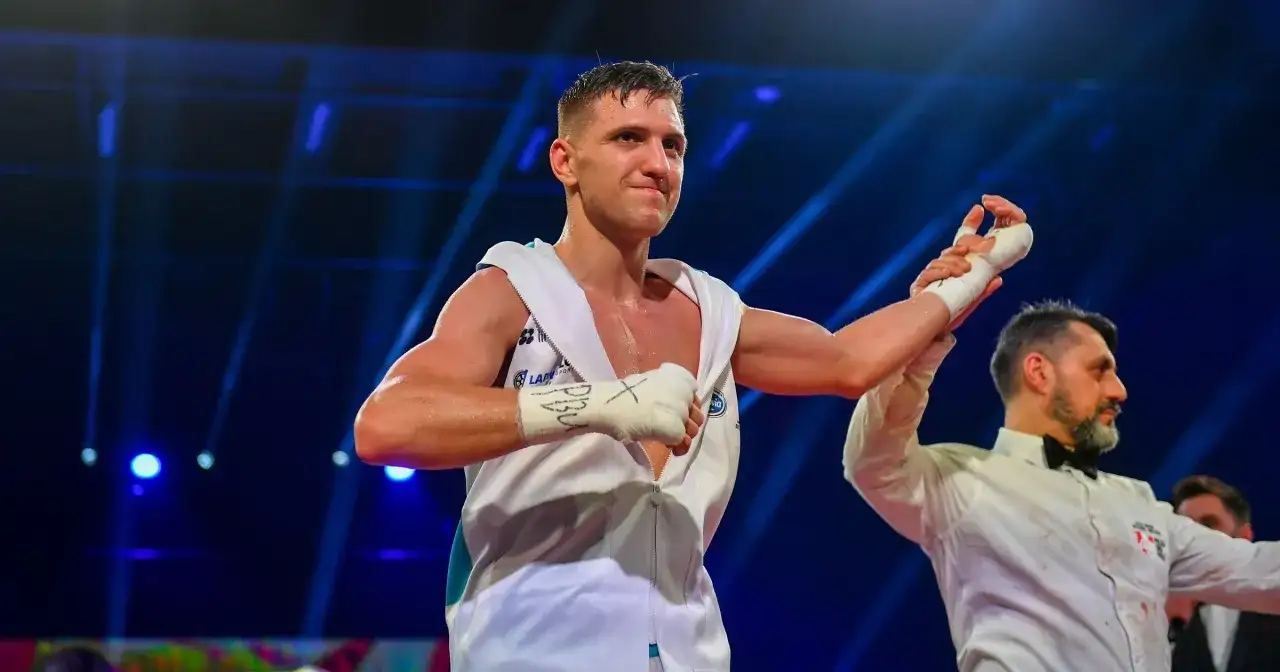 Bokser w białej szacie z podniesioną ręką, obok sędzia w białej koszuli.