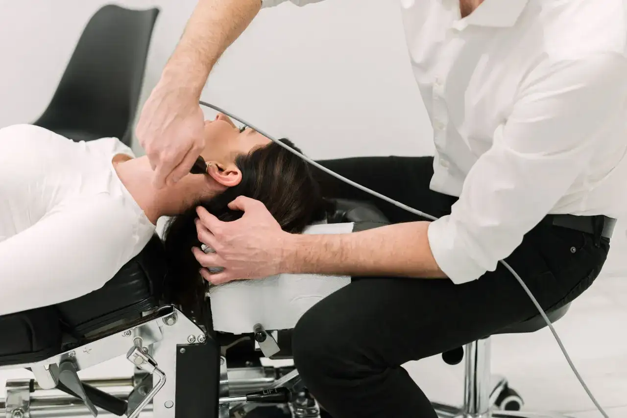 Chiropraktyk wykonuje zabieg na szyi pacjentki leżącej na kozetce.