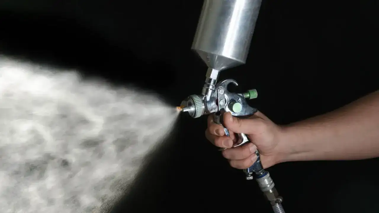 Dłoń trzymająca pistolet lakierniczy rozpylający mgiełkę.