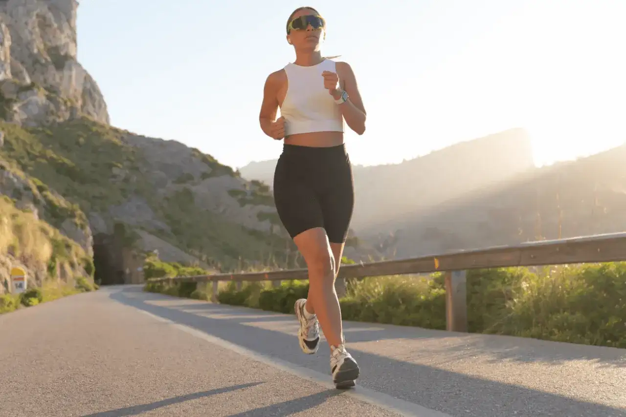Kobieta biegnie po górskiej drodze, zastanawiając się, jak często biegać żeby schudnąć. Słońce zachodzi, tworząc piękne światło.