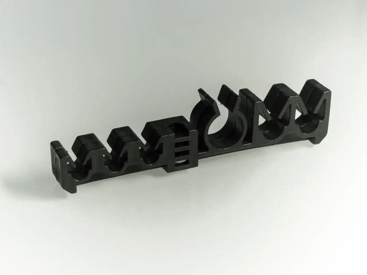 Czarny, plastikowy uchwyt z wieloma otworami, służący do mocowania przewodów hamulcowych.