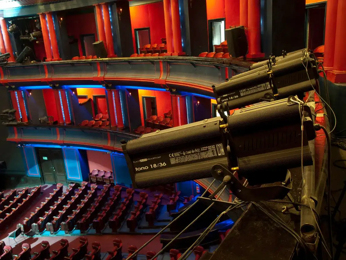 Wnętrze teatru z rzędami czerwonych siedzeń i balkonami. Reflektory oświetlają scenę. Ile miejsc ma teatr roma?