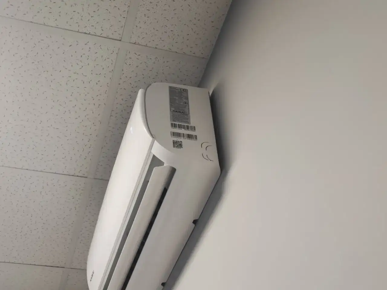 Biała jednostka klimatyzacyjna zamontowana na ścianie pod sufitem podwieszanym.