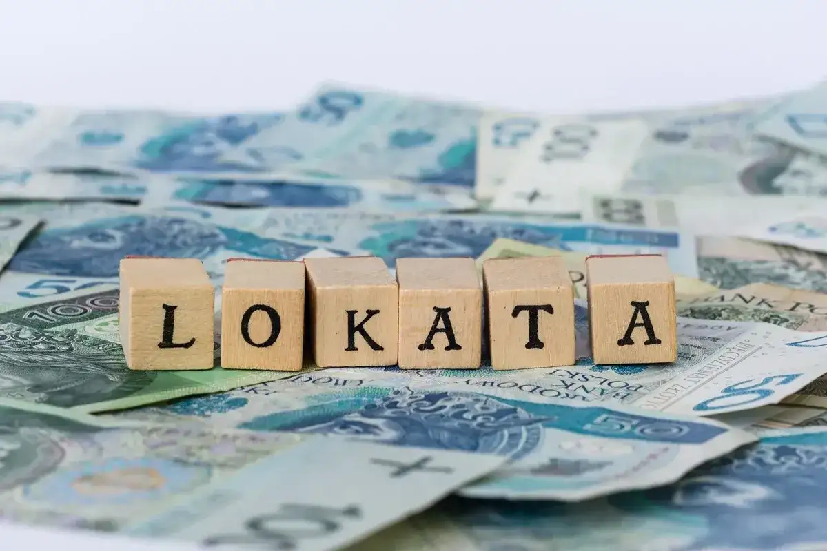 Drewniane klocki z literami "LOKATA" na tle polskich banknotów.