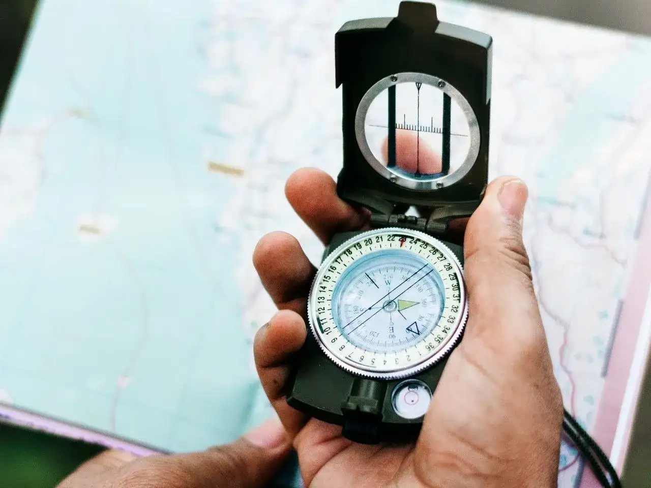 Dłoń trzyma otwary kompas na tle mapy.