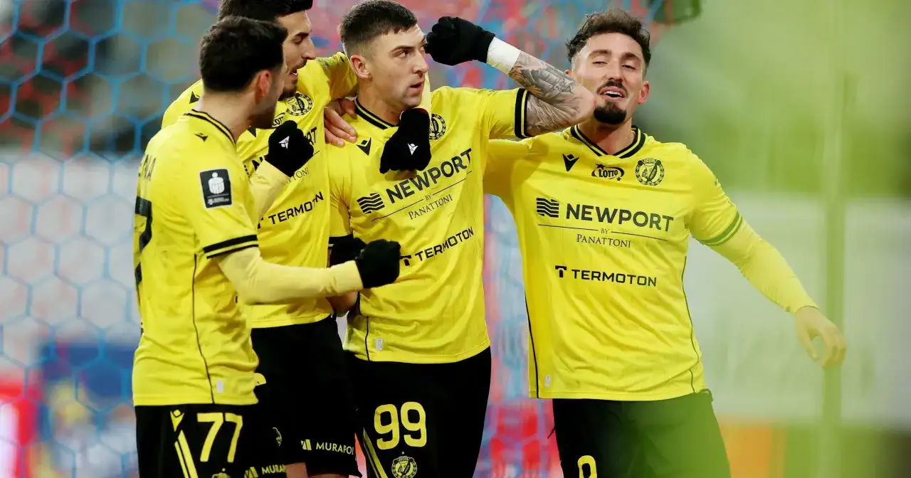 Piłkarze w żółtych koszulkach świętują bramkę. Fani spekulują o plotkach transferowych Widzewa, a drużyna cieszy się sukcesem.