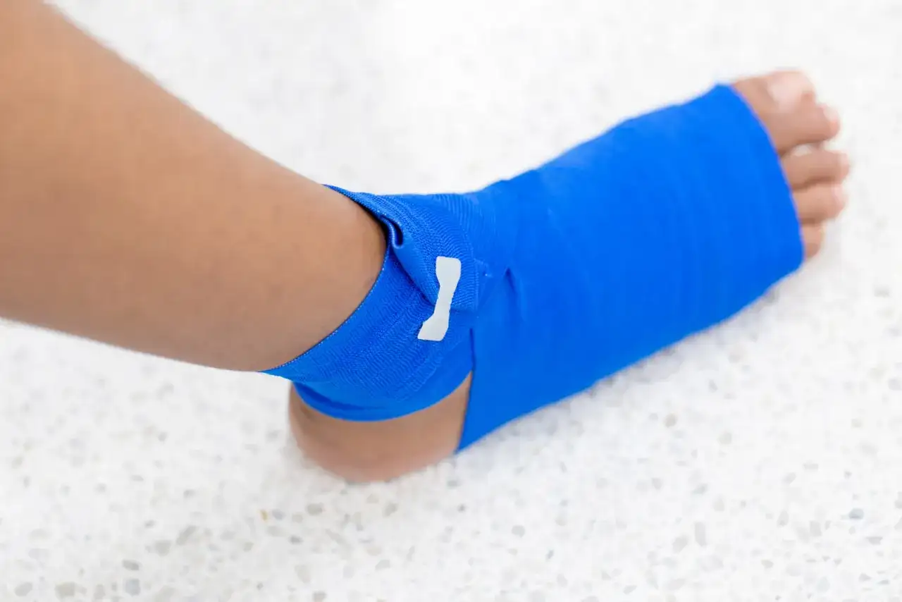 Noga z zabandażowaną niebieską opaską kostką.