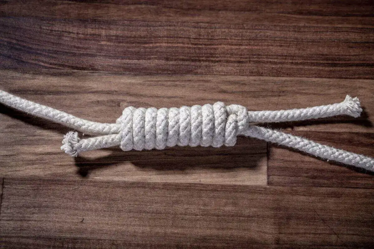 Zbliżenie na węzeł łączący dwie białe liny na drewnianym tle.